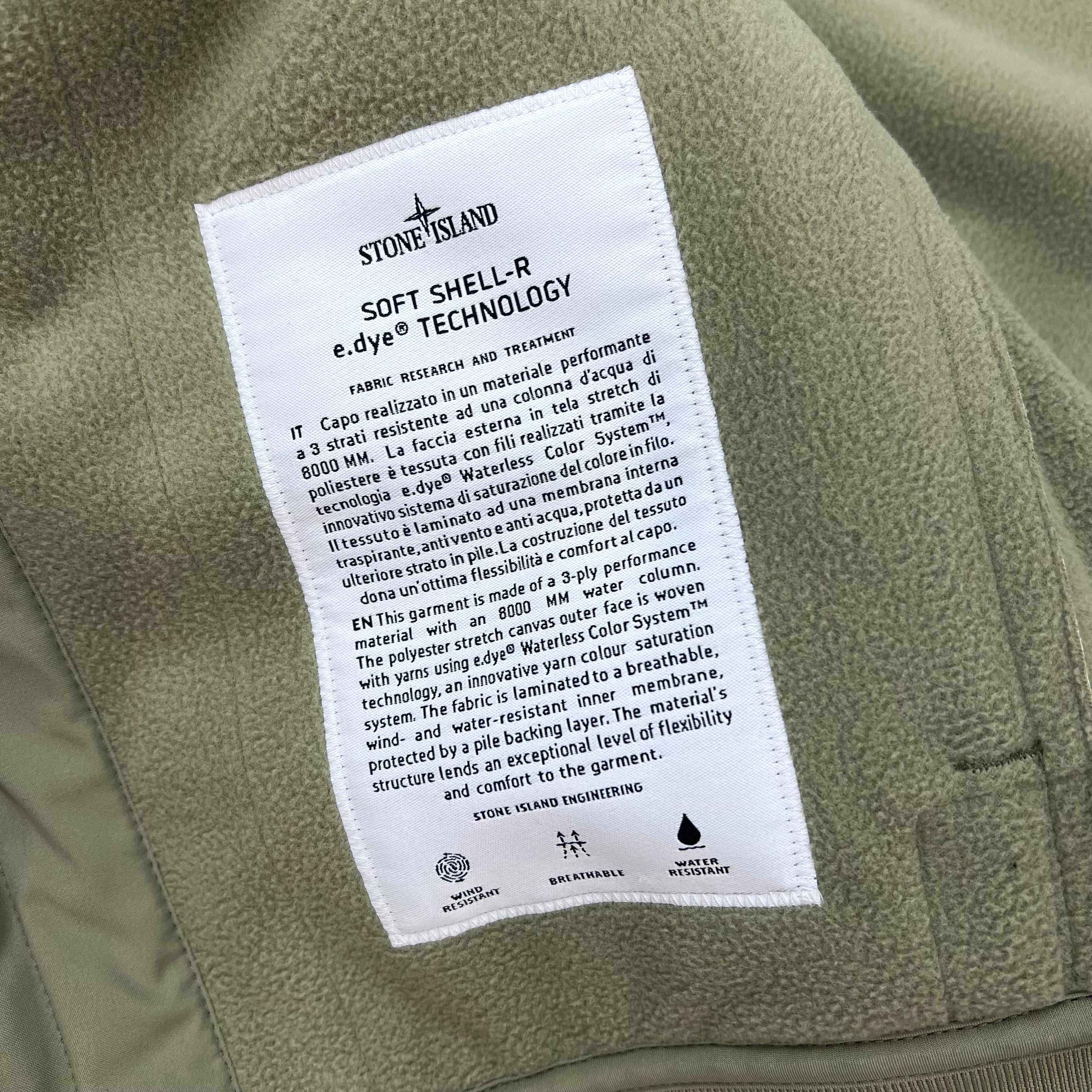 A close up view of the engineering label on the inside of a Stone Island Soft Shell-R_e.dye® Jacket in Laurel Green.