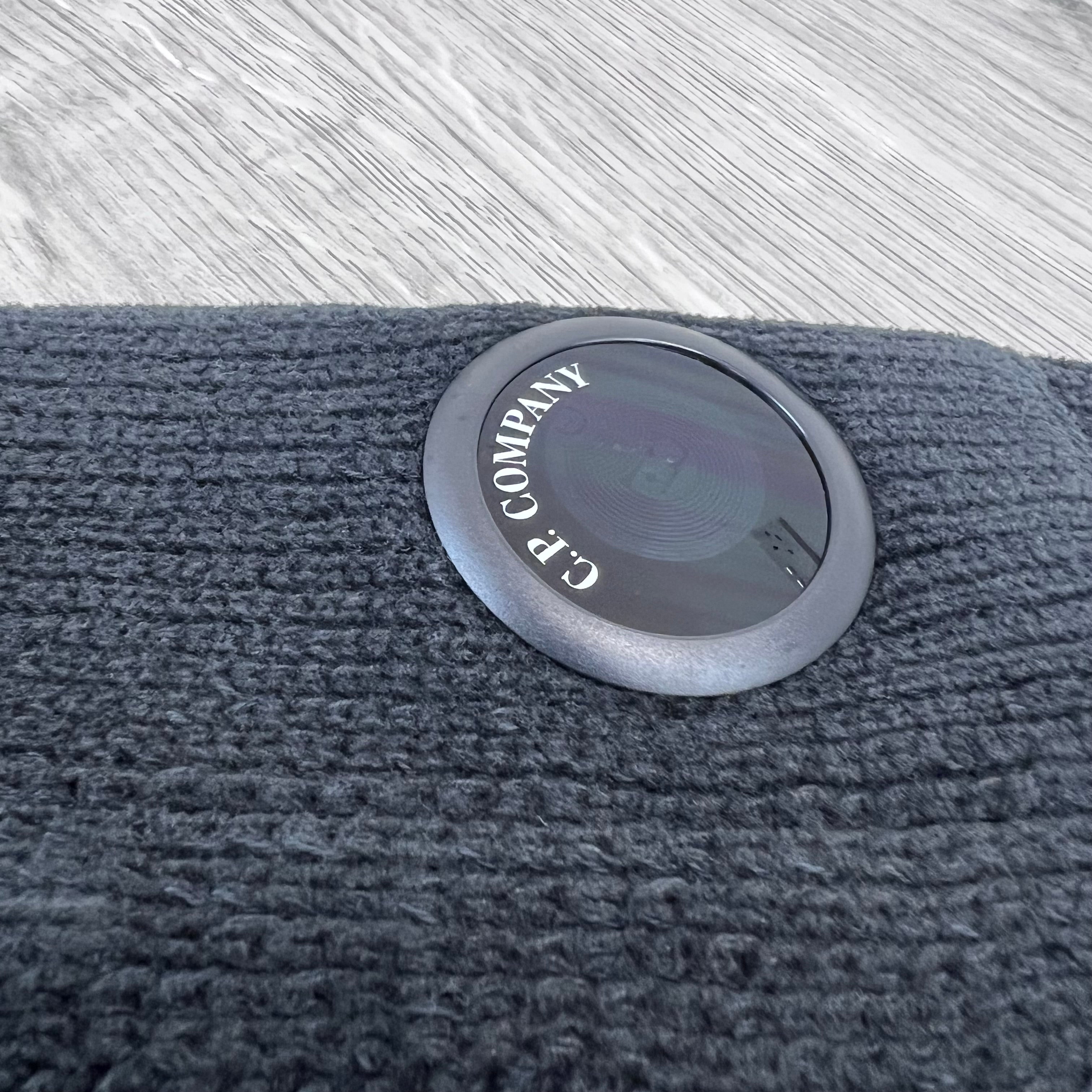 A close up view of the plastic sleeve lens on a CP Company Chenille Cotton Lens Sweatshirt in Black. 