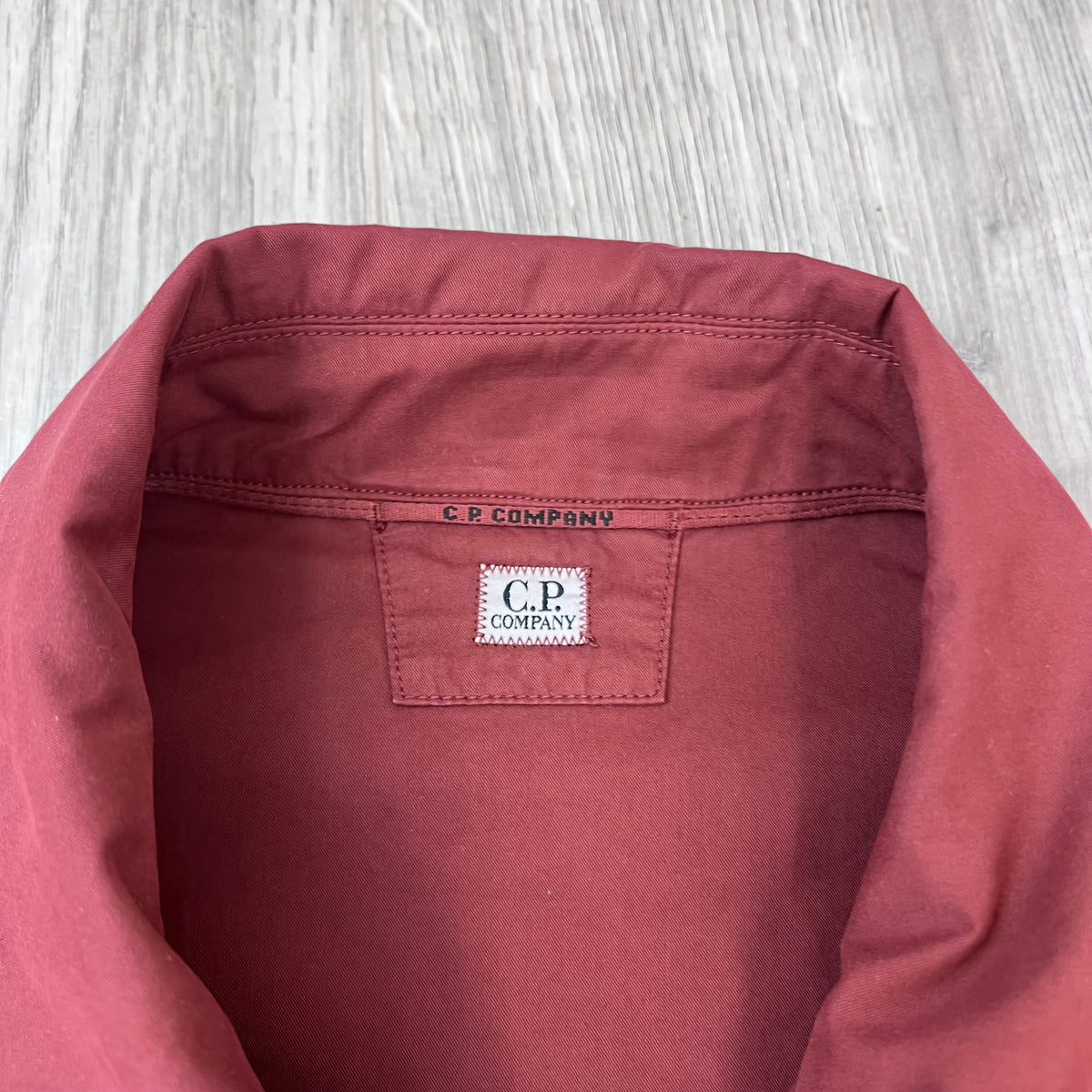 Close up view of the neck label on the CP Company Zip Overshirt in Andorra Red. 
