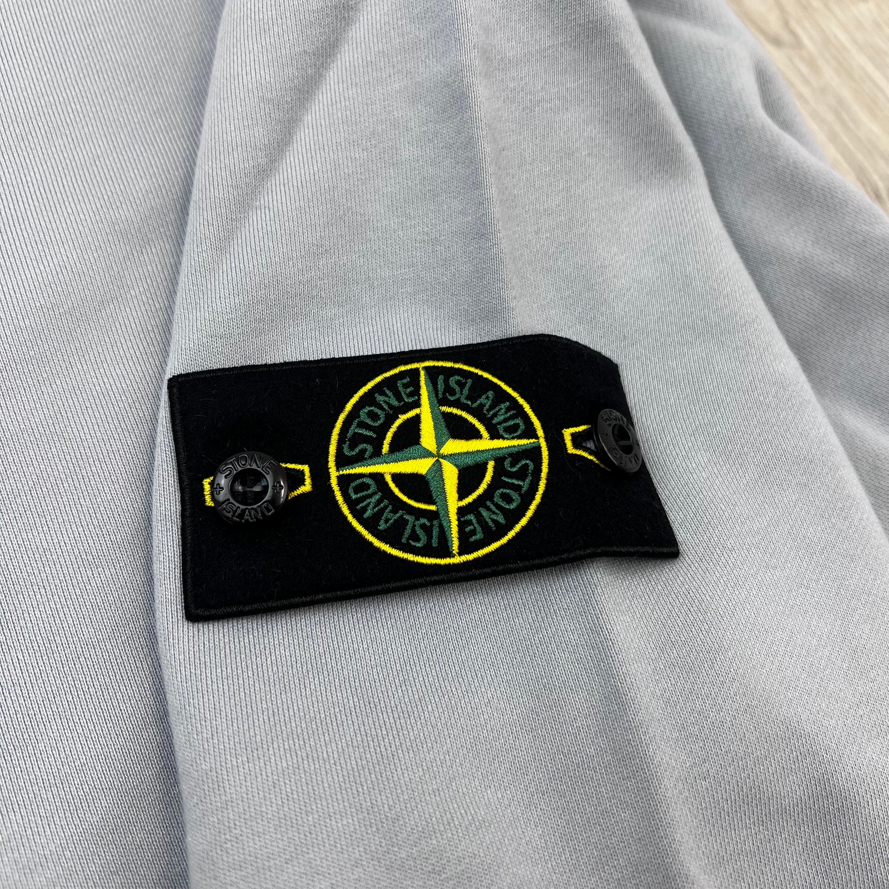 A close up view of the badge logo on a Stone Island Crewneck Sweatshirt in Ash Grey.