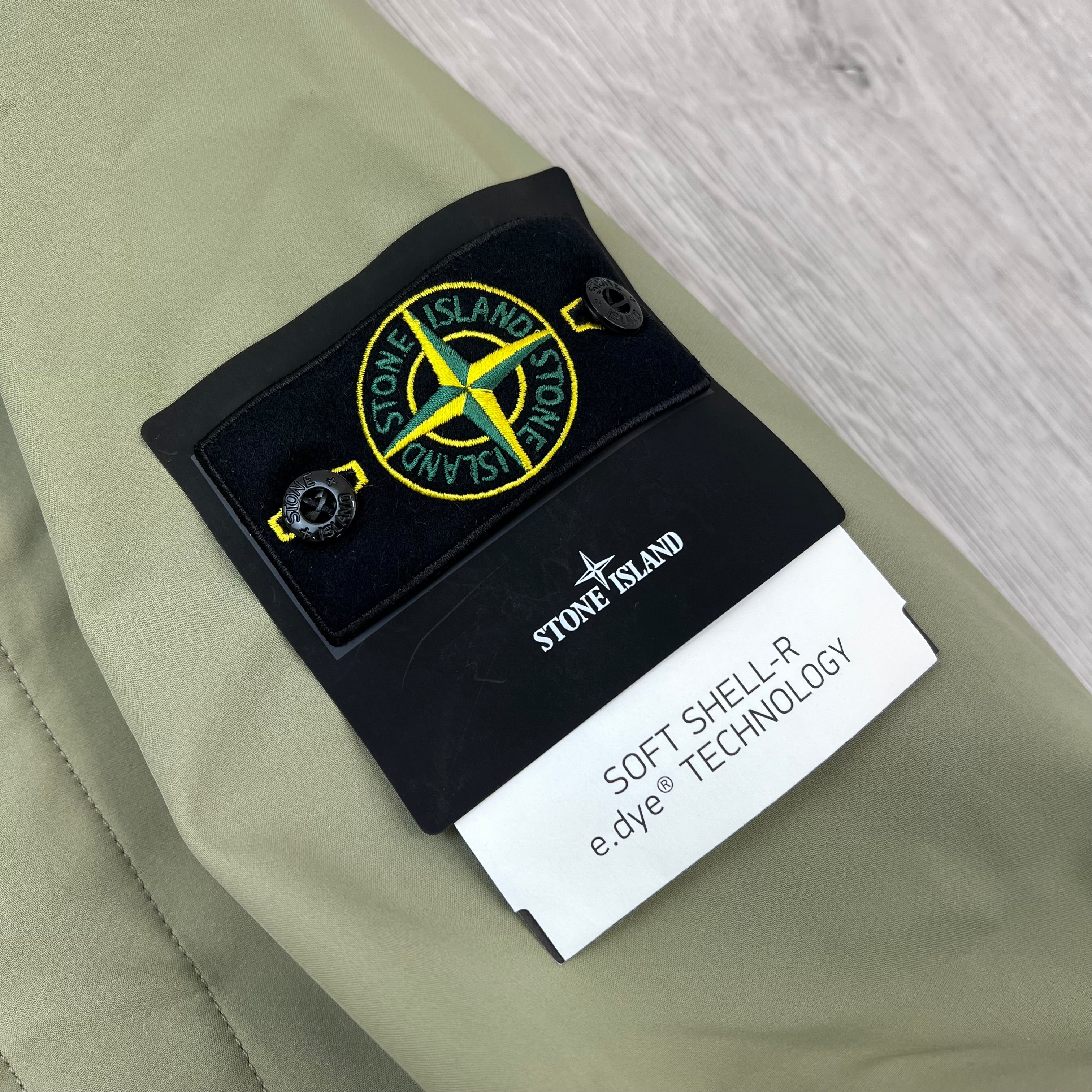 A close up view of the badge logo on the sleeve of a Stone Island Soft Shell-R_e.dye® Jacket in Laurel Green.